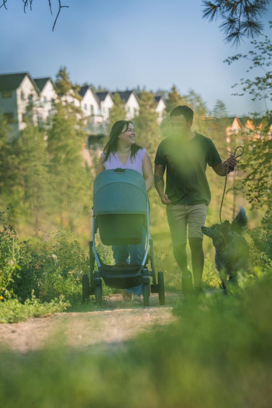 Couple with stroller and dog walking in park with townhomes in background