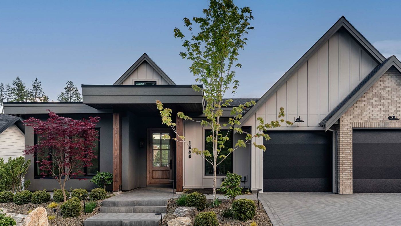 Rykon Hidden Hills showhome front entrance with brick and wood accents, landscaped pathway, and mature trees in Wilden, Kelowna